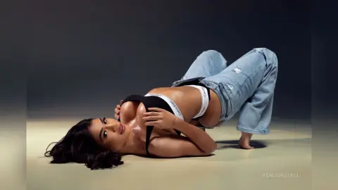 Brunette woman in black Calvin Klein bra and denim jeans lying on a studio floor with a moody aesthetic.