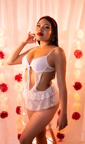 Young woman in white lace lingerie posing against a warm floral backdrop with a romantic mood.