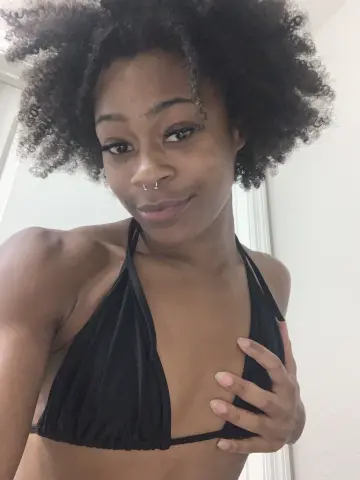 Smiling young woman with natural afro hair wearing a black bikini top in a bright indoor setting.