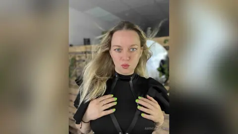 Blonde woman in a stylish black puff-sleeve top posing with a confident expression in a bright indoor setting.