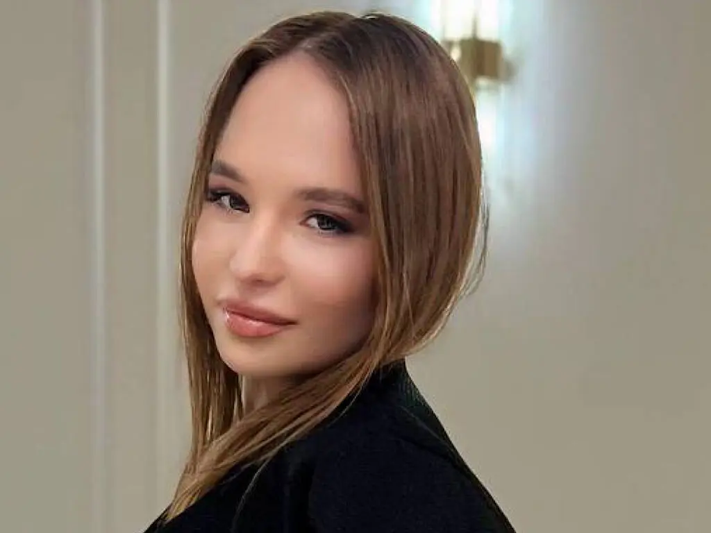 Portrait of a smiling young woman with long brown hair wearing a black top in a bright indoor setting.