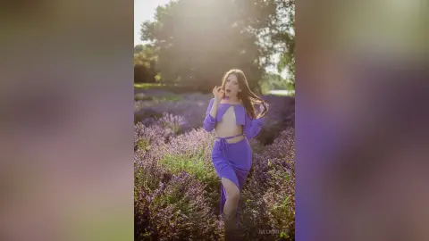 Dreamy portrait of a woman in a purple crop top and skirt standing in a blooming lavender field at sunset.