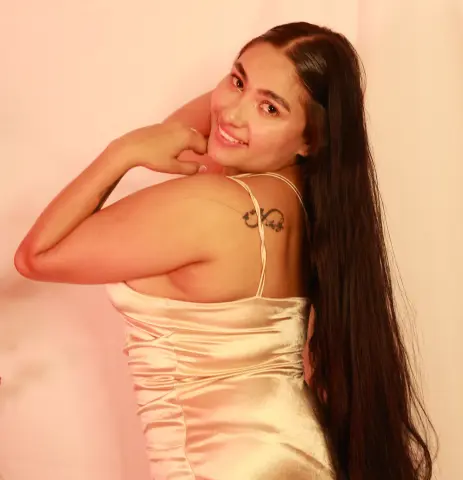 Smiling young woman in a champagne satin slip dress posing against a warm pink studio background.