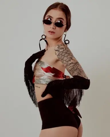 Stylish woman in a red patterned tube top and black velvet gloves with large hoop earrings and tattoos.