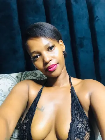 Smiling Black woman in a black lace halter top relaxing against a dark velvet backdrop.