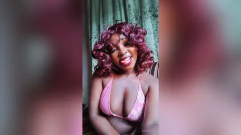 Smiling woman with curly reddish hair wearing a pink bikini in a cozy indoor setting.