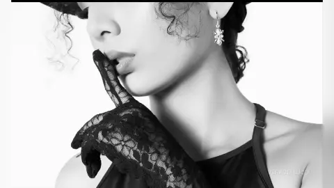 Elegant woman in black lace gloves and floral earring posing in a moody black and white portrait.