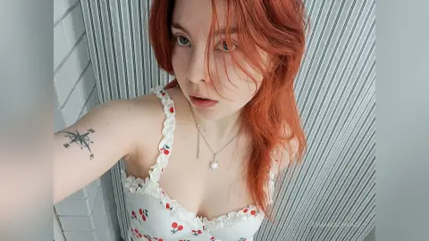 Redheaded woman in a white floral sundress with a compass tattoo posing in a bright indoor setting.