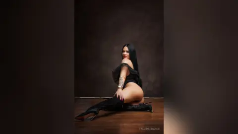 Elegant woman in a black bodysuit and high boots posing against a dark studio background.