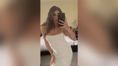 EmmaFitzgerald poses for a mirror selfie wearing a tight white spaghetti-strap dress that accentuates her curves.