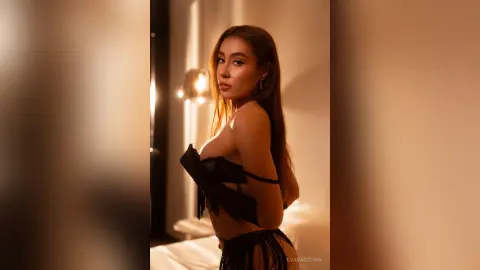 Glamorous woman in a black strapless corset top posing in warm, moody indoor lighting.