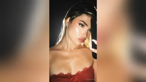 Glamorous woman in a red lace camisole taking a glowing selfie in dim lighting.
