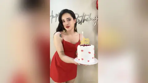 Young woman in a red dress celebrating her birthday with a white cake in a festive indoor setting.