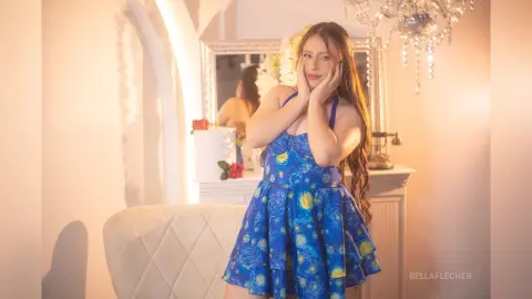 Young woman in a blue floral sundress posing in a warm, sunlit room with vintage decor.