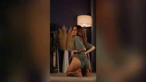 Young woman in a green loungewear set posing in a moody, dimly lit room with pampas grass decor.