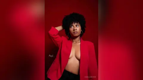 Confident woman with curly hair wearing a red blazer against a bold red background.