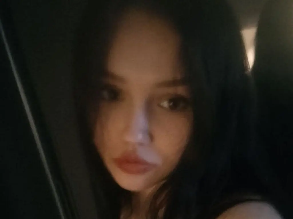 Close-up portrait of a young woman with long dark hair in moody, low-light indoor setting.