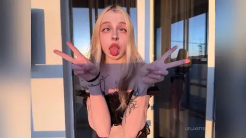 Blonde woman in a black ruffled top making peace signs on a sunny balcony with a playful mood.