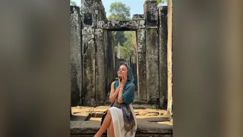 AnaMathers poses outdoors against stone ruins wearing a blue wrap and a white skirt.