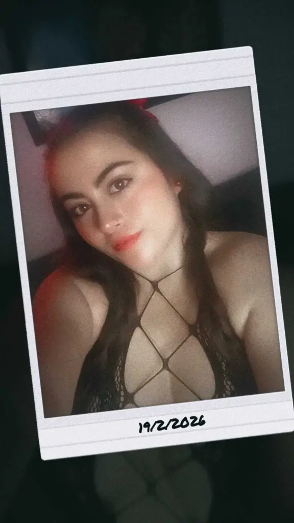 FlirtyAphrodyte looks at the camera with a pouty expression, showing her long dark hair and dangling earrings against a plain white background.