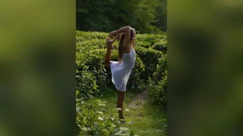Graceful woman in a white summer dress performing a yoga stretch in a lush green tea plantation.