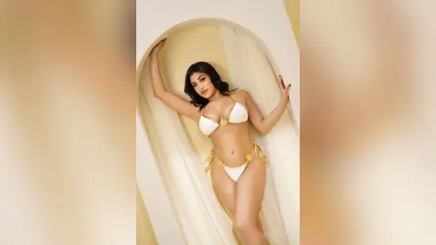 Glamorous woman in a white bikini posing in a sunlit arched doorway for a summer fashion look.