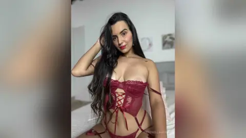 AntonellaJones — Young woman with long dark hair wearing burgundy lace lingerie in a bright, minimalist bedroom setting.