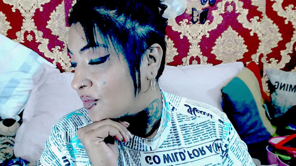 Close-up portrait of a woman with winged eyeliner, nose ring, and neck tattoos looking into the camera.