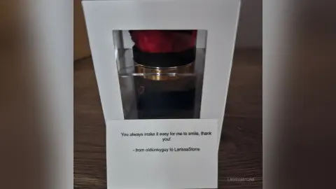 Gift box containing a luxury red and black item with a sentimental thank you note on a wooden surface.