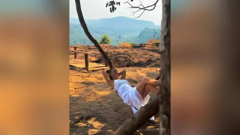 AnaMathers reclines on a dirt path in a white sundress with her hands behind her head.