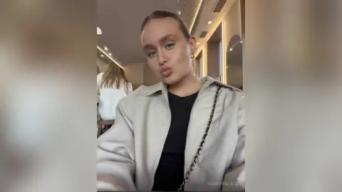 BonnyWalace pouts at the camera while wearing a beige jacket and black top in a brightly lit room.