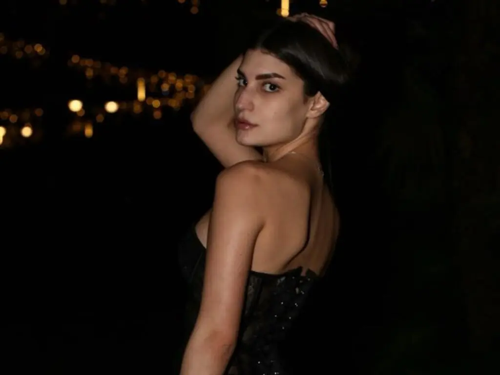 Elegant woman in a black corset dress posing against a dark night background with soft bokeh lights.