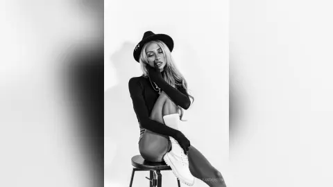 LeslyAnderson poses sitting on a stool wearing a black long-sleeved top and white shorts.