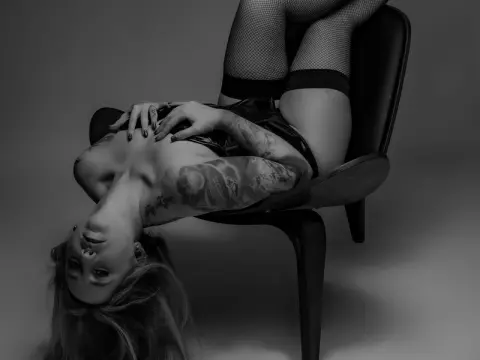 Moody black and white portrait of a tattooed woman in fishnet stockings reclining on a chair.