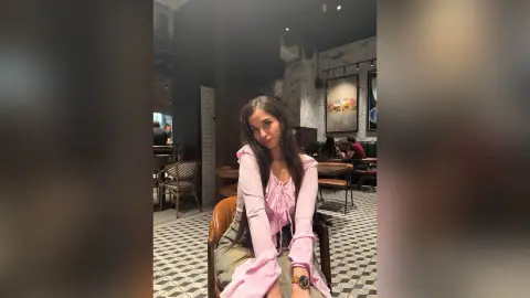 Young woman in a pink ruffled blouse sitting in a modern cafe with patterned tile flooring.