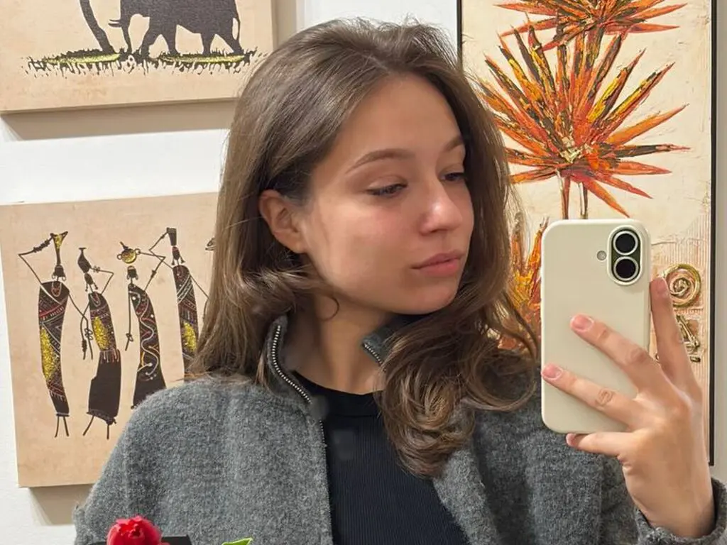 AnnaMariardi takes a selfie wearing a grey zip-up jacket and a black top, looking into her phone camera.