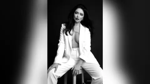 Elegant woman in a white power suit posing against a black background in a sophisticated studio portrait.