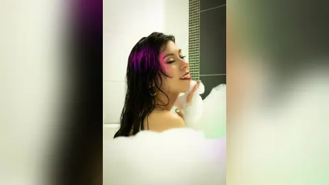 SamanthaHarvey poses in a white bathtub filled with thick white bubbles, showing her bare shoulders and wet dark hair.