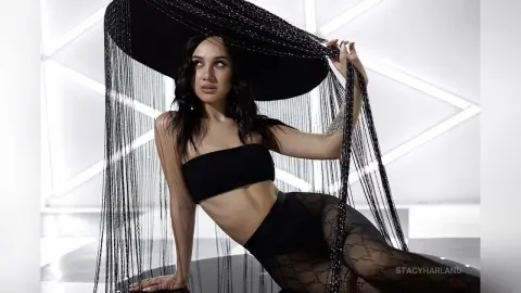 Elegant woman in a black strapless top and sheer tights wearing a dramatic black sequined fringe wide-brim hat.
