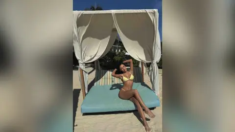 Relaxed woman in a yellow bikini lounging on a cabana bed at a sunny tropical beach resort.