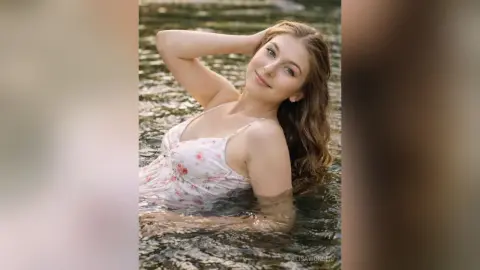 Young woman in a white floral sundress relaxing in a serene river during a peaceful summer day.