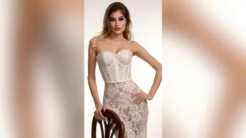 Elegant woman in a white lace corset midi dress posing against a neutral studio background.