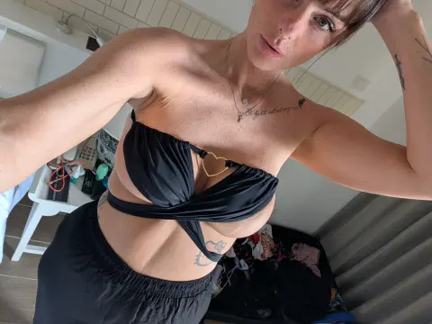 Young woman in a black bikini top and shorts posing for a selfie in a bright indoor setting.