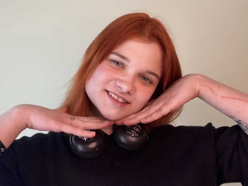 Smiling redhead woman in a black sweater wearing headphones against a neutral background.