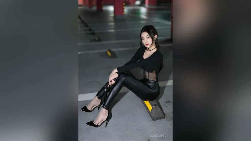 AliceBabson poses in a black long-sleeved top and tight black leggings while squatting on a concrete parking garage floor.
