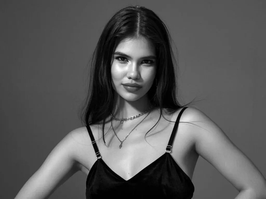 CelesteDecket poses in a black camisole with long dark hair and silver necklaces against a plain grey background.