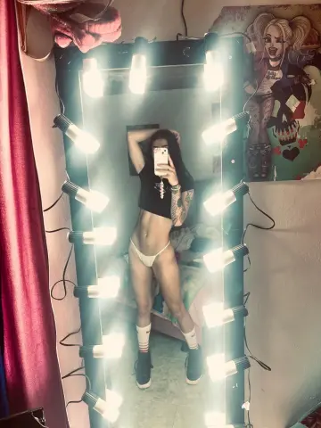Fit woman in black crop top and white bikini bottoms posing in a lit vanity mirror for a confident selfie.