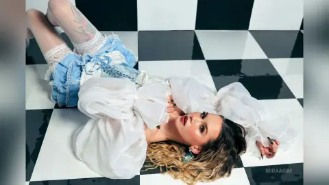 Fashionable woman in a white blouse and blue denim shorts lying on a black and white checkered floor.