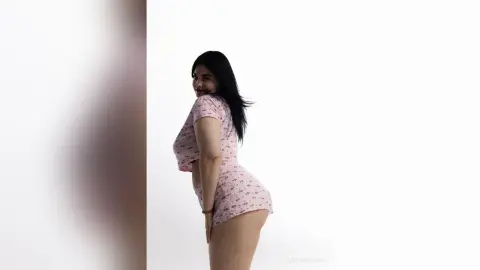 Smiling woman in a pink floral romper posing against a white background in a bright, minimalist setting.