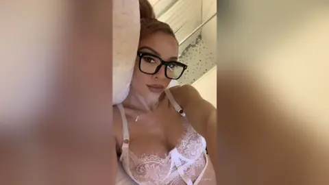 KendallMinx wearing black glasses and white lace lingerie while lounging in bed.